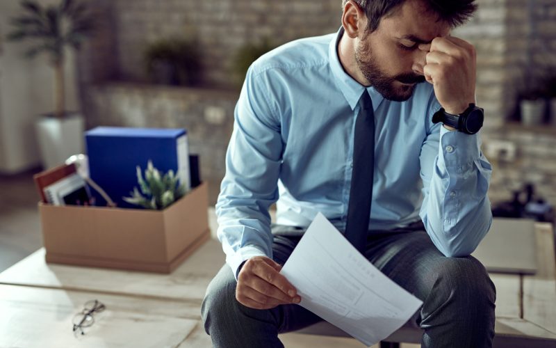 Young frustrated businessman holding his head in pain after being fired at work.